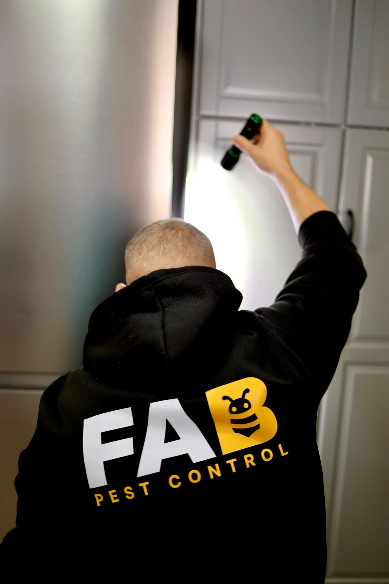 FAB Pest Control technician inspecting a Perth kitchen cabinet with a torch