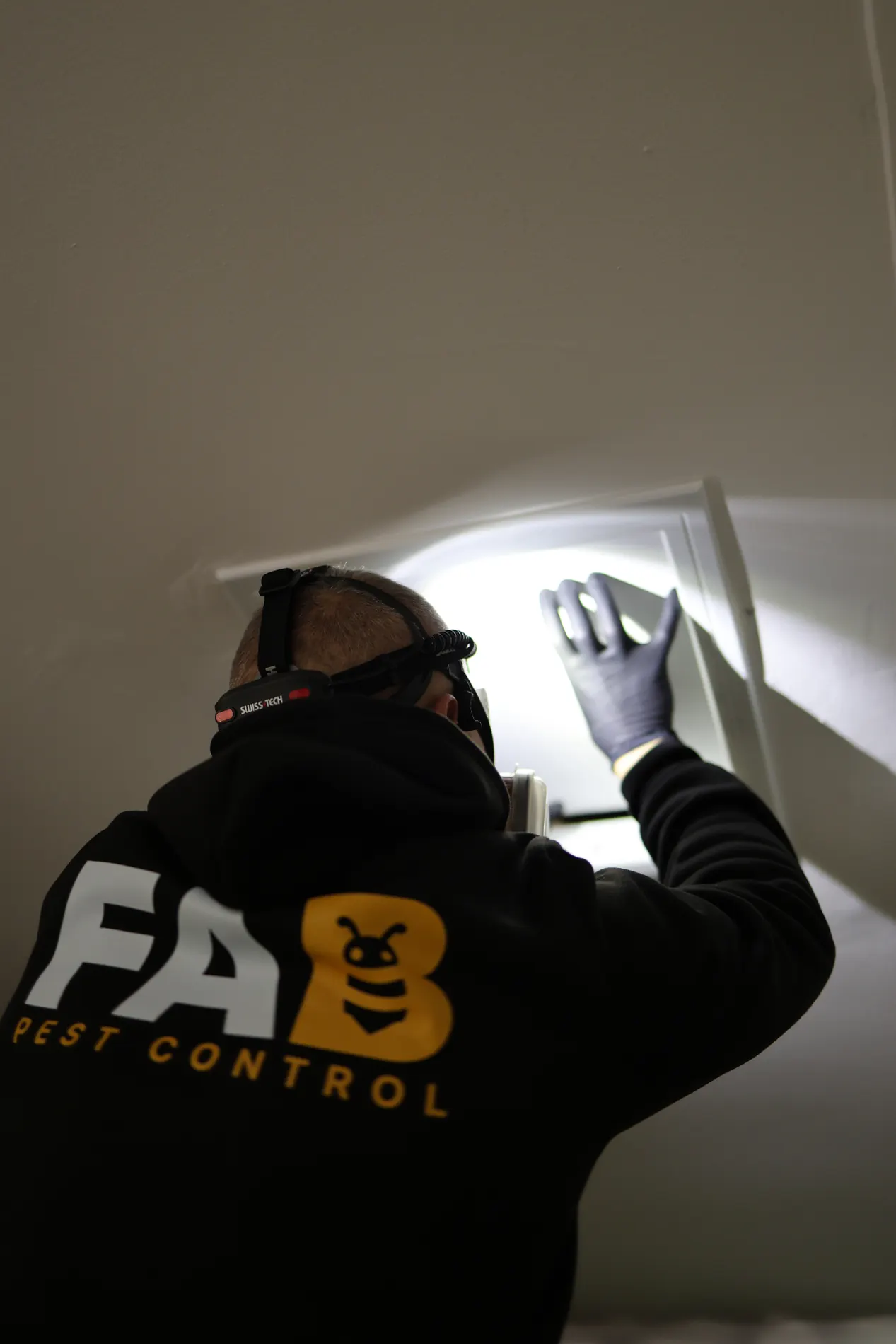 FAB Pest Control technician inspecting a Perth roof void access hatch with a headlamp