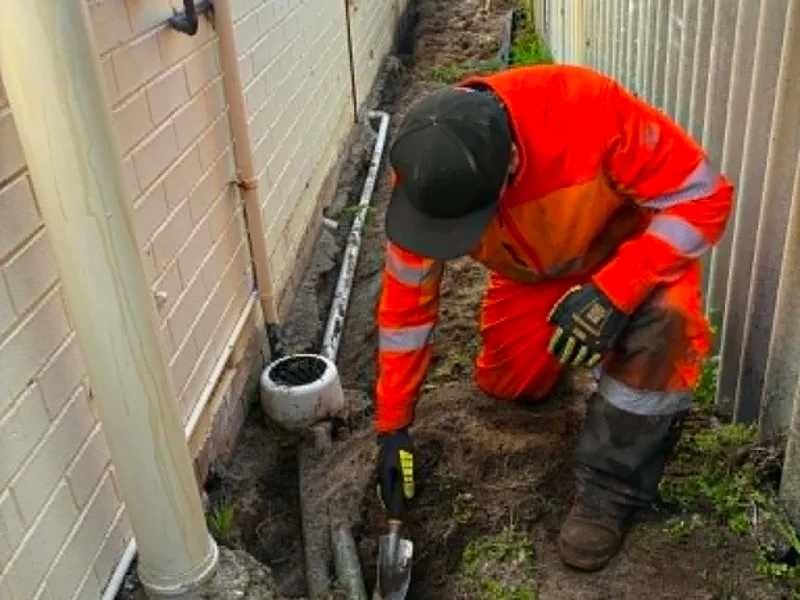 FAB Pest Control technician inspecting beside an external wall and pipework for termite risk